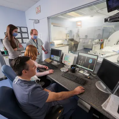Healthcare workers observe a diagnostic exam using an MRI machine.