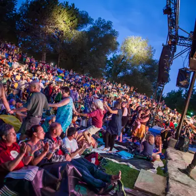 A large crowd dancing outdoors while enjoying a performance at the Summerfolk music festival.