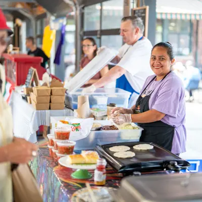 A woman smiles while serving food at a farmers' market