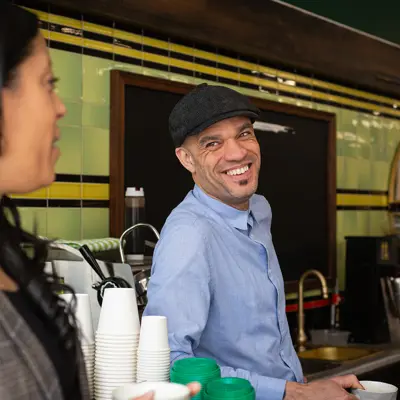 A cafe owner in a blue shirt smiles while leaning over the counter.